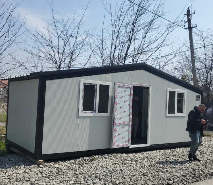სენდვიჩ პანელის კოტეჯი მოხრეშილ ზედაპირზე, ღია კარით, წინა ფასადის ფოტო